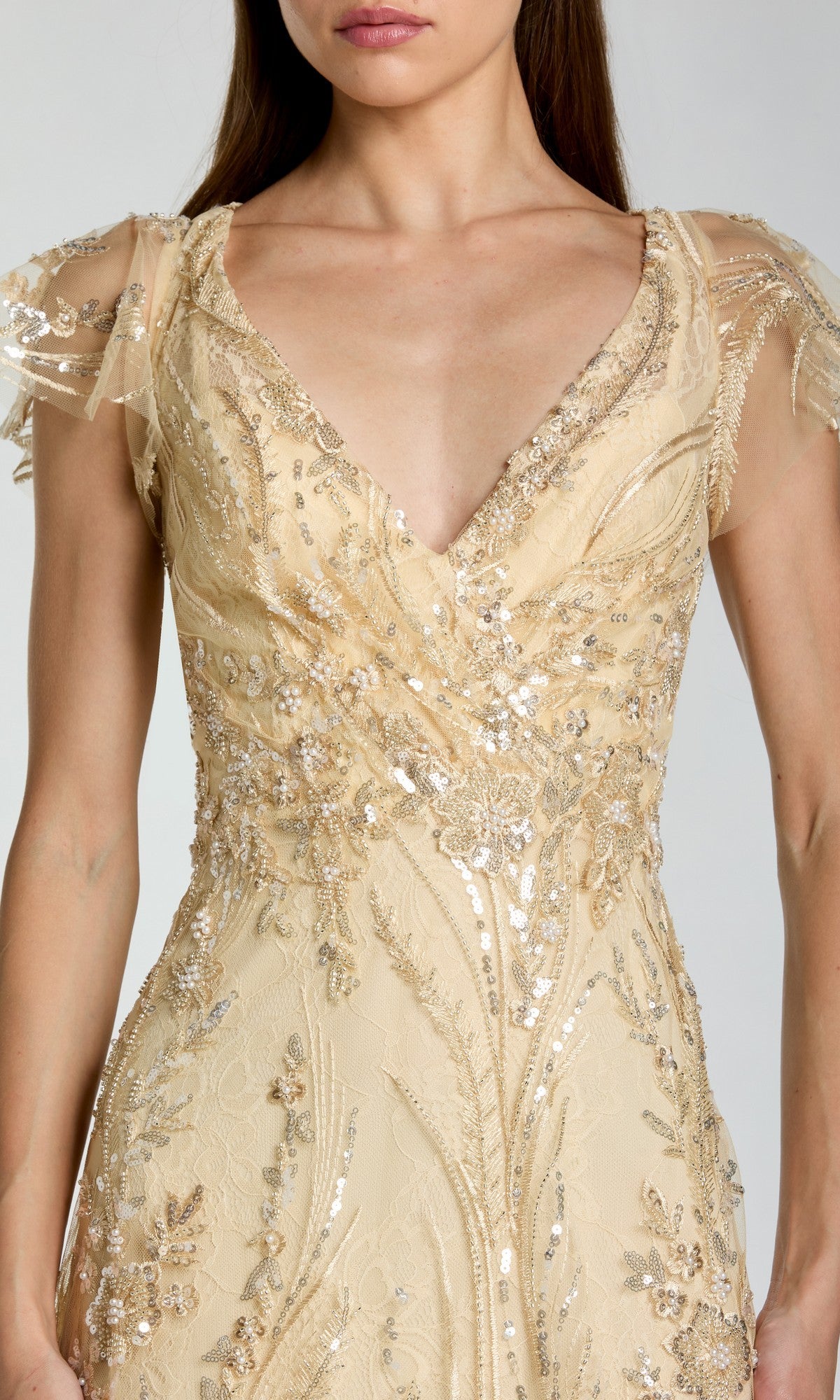 A woman wearing the Mac Duggal 68914 long formal dress in light gold, featuring intricate sequin and bead embroidery, sheer short sleeves, and a deep V-neckline.